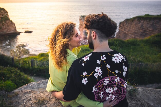 Young heterosexual couple embracing each other at the top of a cliff near the ocean.