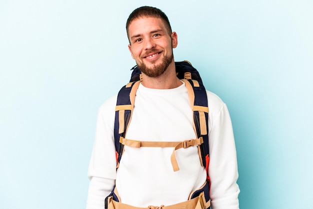 Young hiker caucasian man isolated on blue background happy, smiling and cheerful.