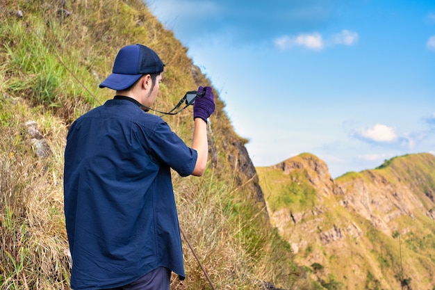 Young hiker taking a photography along path of terkking. Photographer taking photo at mountain peak.