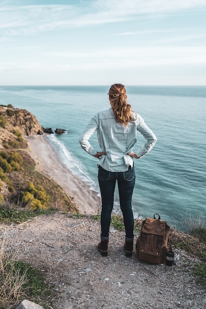 Young hip woman with a backpack explores the coast on a beautiful day. Concept of exploration and adventures