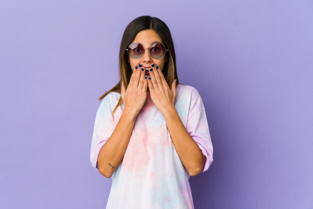 Young hippie woman isolated on purple background shocked, covering mouth with hands, anxious to discover something new.