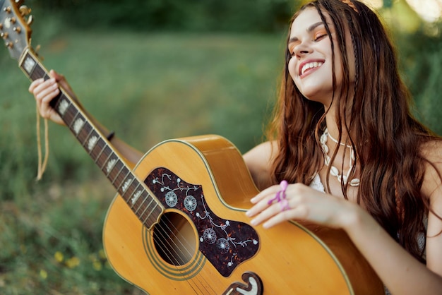 Young hippie woman with eco image smiling and looking into the\
camera with guitar in hand in nature on a trip
