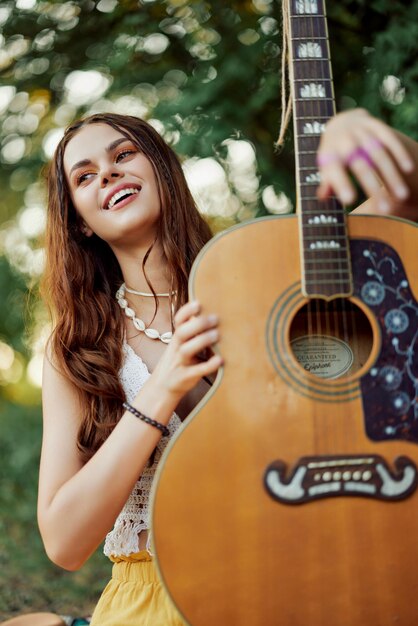 Photo a young hippie woman with a guitar in her hands smiles sweetly into the camera on a trip to nature lifestyle in harmony high quality photo