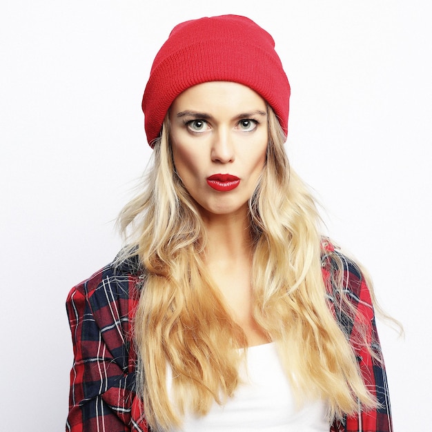 Young hipster blonde woman with bright sexy make up wearing stylish urban plaid shirt and red hat