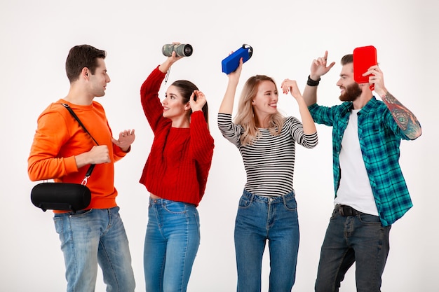 Foto compagnia di giovani hipster di amici che si divertono insieme sorridendo ascoltando musica su altoparlanti wireless, ballando ridendo isolato muro bianco in vestito elegante colorato