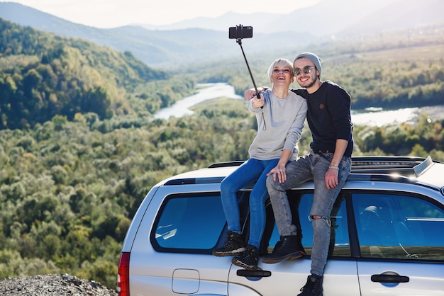 Giovani coppie dei pantaloni a vita bassa nell'amore che fa selfie facendo uso dello smart phone