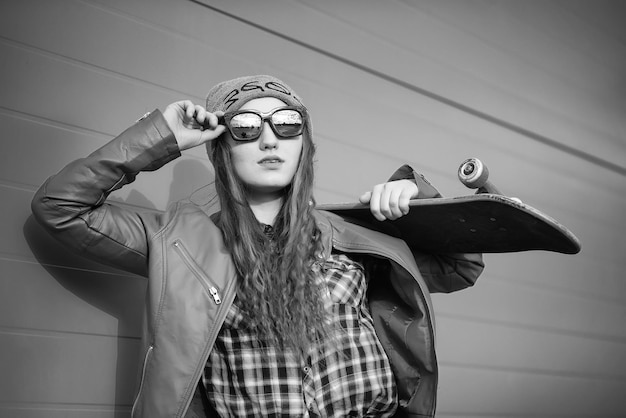 A young hipster girl is riding a skateboard Girls girlfriends for a walk in the city with a skateboard Spring sports on the street with a skateboard