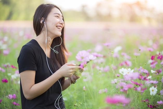 コスモスの花畑でヘッドフォンで音楽を聴いている若いヒップスターの女の子。リラックスのコンセプト。