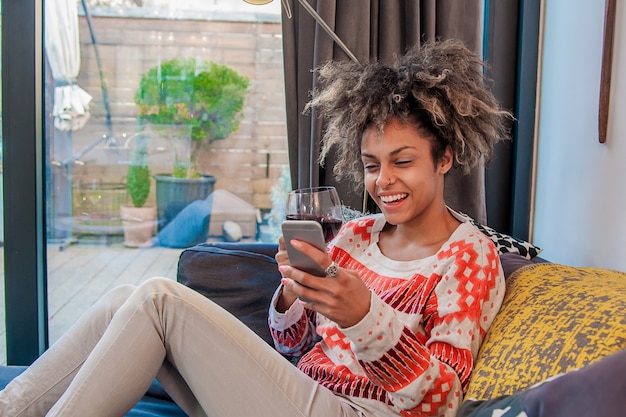 Young hipster girl using modern smartphone device while sitting at home and communicate with friends in social networks,female freelancer working from home, happiness and enjoyment lifestyle