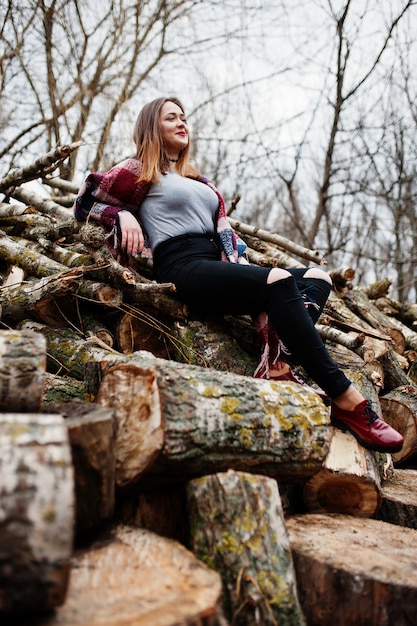 Young hipster girl wear on blanket against wooden stumps on wood.