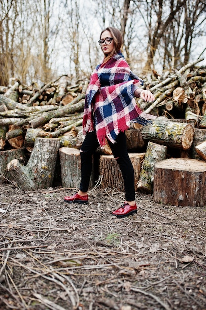 Young hipster girl wear on blanket and glasses against wooden stumps on wood.