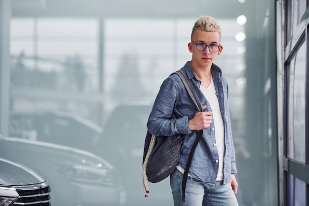 Young hipster guy in nice clothes stands indoors near modern car