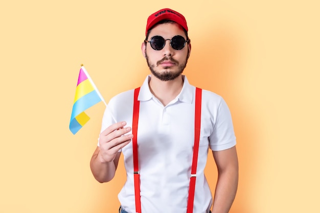 Young hipster holding Pansexual pride community flag on light orange background