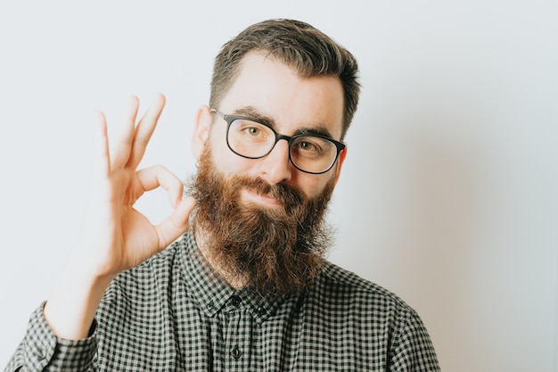 A young hipster male with blue light glasses looking to camera while making the OK sign