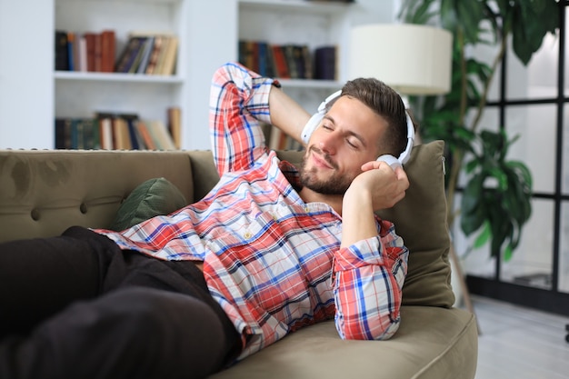 Young hipster man lies on the couch and listens to music in wireless headphones.