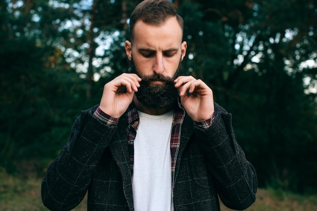 Young hipster man straightens his mustache in the forest