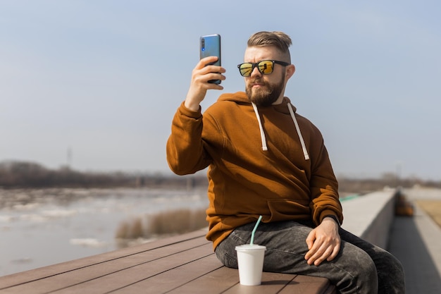 Young hipster man using smart phone sitting on wooden boards social media communication