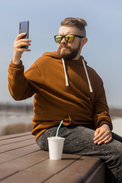 Young hipster man using smart phone sitting on wooden boards social media communication