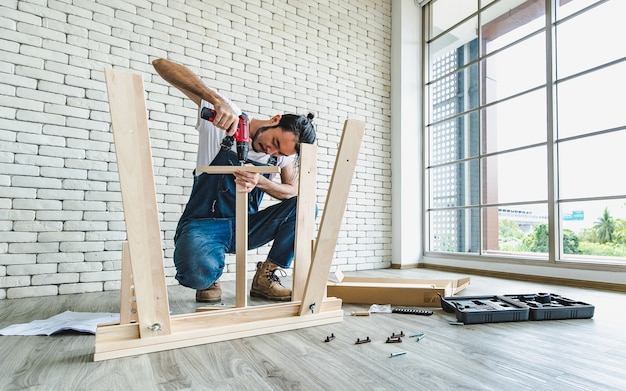 Young hipster man working as handyman, assembling wood table with equipments.