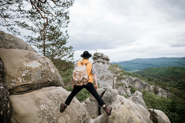 Un giovane viaggiatore hipster si trova tra due rocce e guarda in lontananza