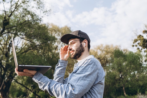 写真 晴れた日に公園でコンピューターを使用して作業しているハンサムな男の外でラップトップコンピューターを使用して若いヒップスター