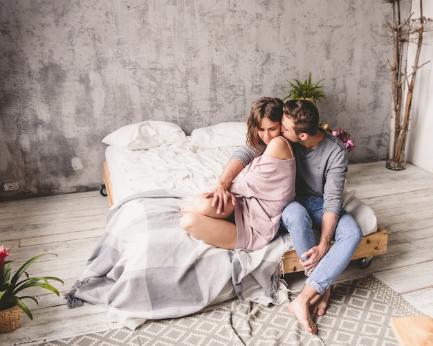 young hipster with beard and attractive woman resting at home while sitting on bed at home