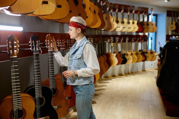 Young hipster woman choosing acoustic guitar in instrument shop. Female buyer at musical store