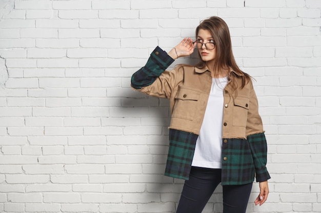 Young hipster woman in eyeglasses over white brick wall. Portrait with copyspace.