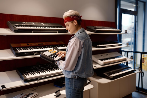 Young hipster woman holding and playing electronic mini piano at music shop store. Purchase at musical workshop sound studio concept