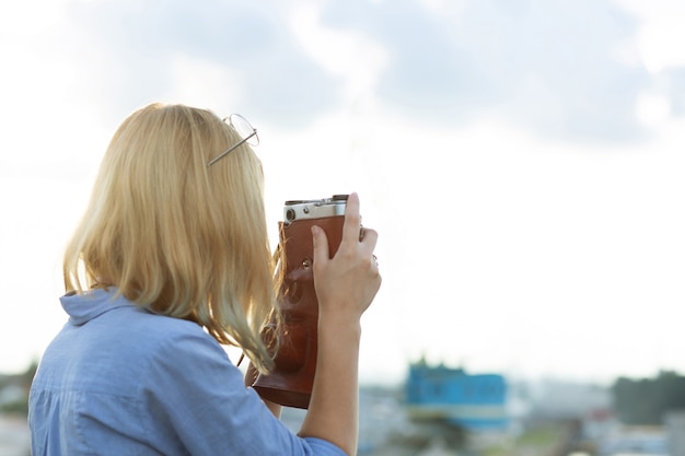 해질녘 빈티지 필름 카메라로 사진을 찍는 파란색 셔츠를 입은 젊은 힙스터 젊은 여성 사진사. 빈 공간