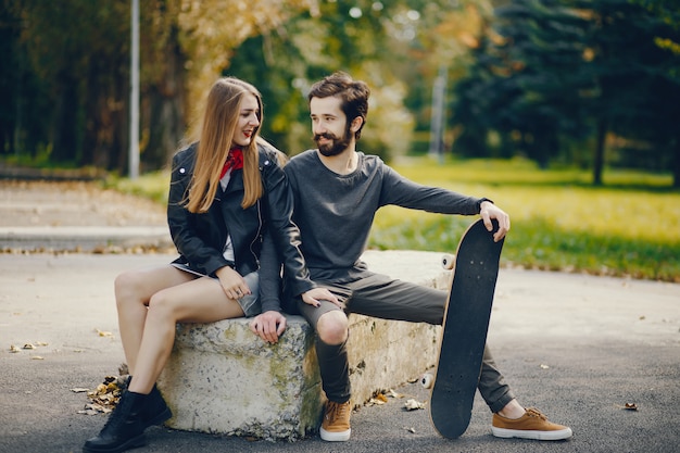 young hipsters sitting in a summer sunny park with a skateboard in their hands