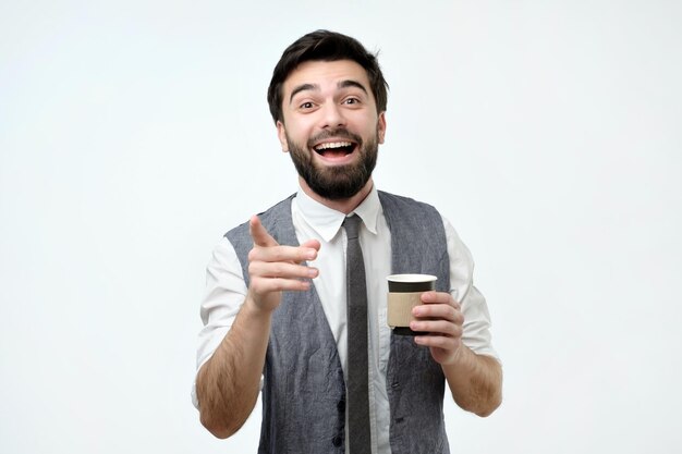 Young hispanic business man pointing at you holding a cup with coffee