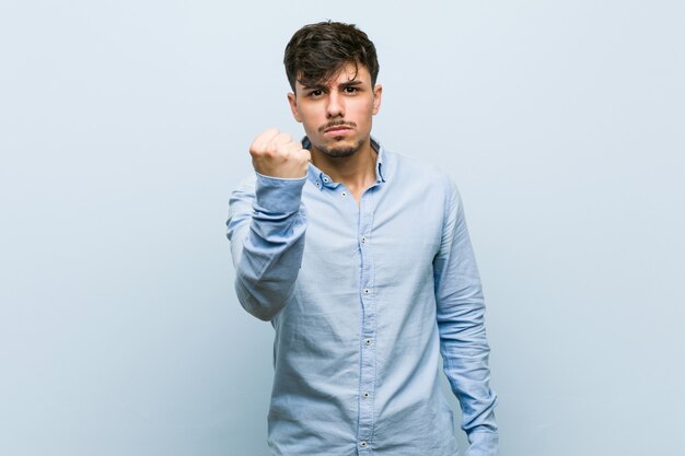 Young hispanic business man showing fist to camera, aggressive facial expression.