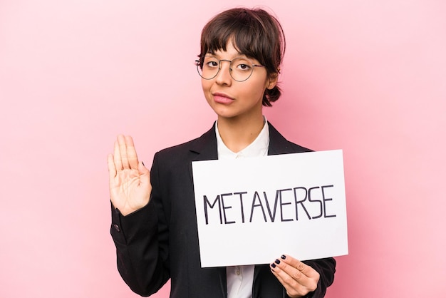 Young hispanic business woman holding a metaverse placard isolated on pink background standing with outstretched hand showing stop sign preventing you