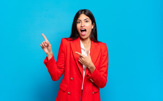 Young hispanic businesswoman feeling joyful and surprised, smiling with a shocked expression and pointing to the side