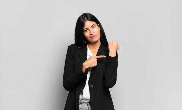 Young hispanic businesswoman looking impatient and angry, pointing at watch, asking for punctuality, wants to be on time