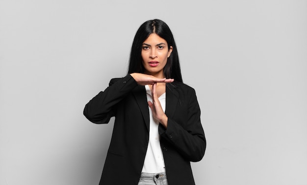 Young hispanic businesswoman looking serious, stern, angry and displeased, making time out sign