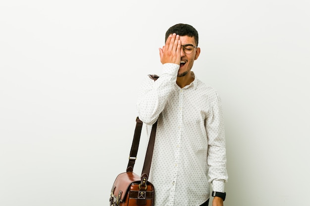 Young hispanic casual business man having fun covering half of face with palm.