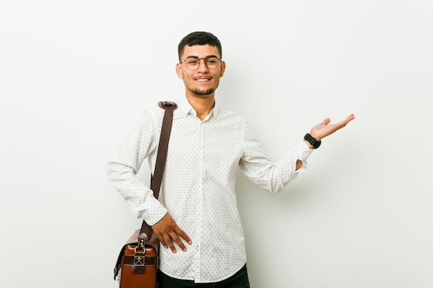 Young hispanic casual business man showing a copy space on a palm and holding another hand on waist.