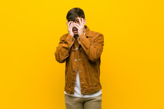 Young hispanic casual man blink through fingers frightened and nervous