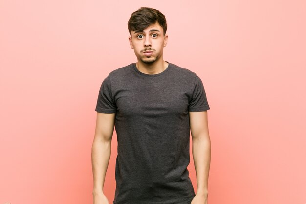 Young hispanic casual man blows cheeks, has tired expression. Facial expression concept.