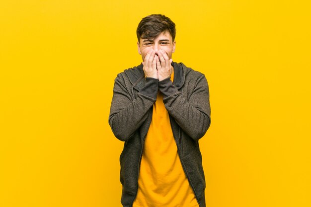 Young hispanic casual man laughing about something, covering mouth with hands.