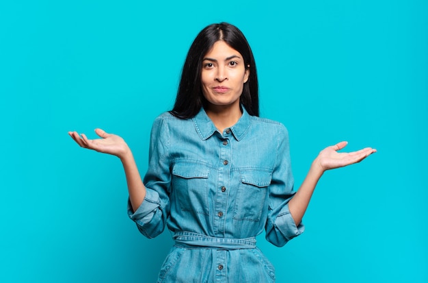 Young hispanic casual woman feeling puzzled and confused, doubting, weighting or choosing different options with funny expression