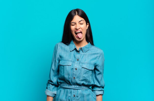 Young hispanic casual woman with cheerful, carefree, rebellious attitude, joking and sticking tongue out, having fun