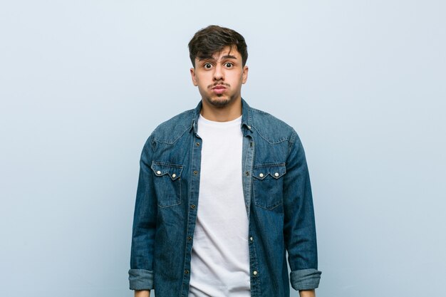 Young hispanic cool man blows cheeks, has tired expression. Facial expression concept.