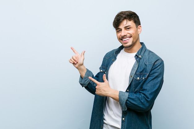 Young hispanic cool man pointing with forefingers to a copy space, expressing excitement and desire.