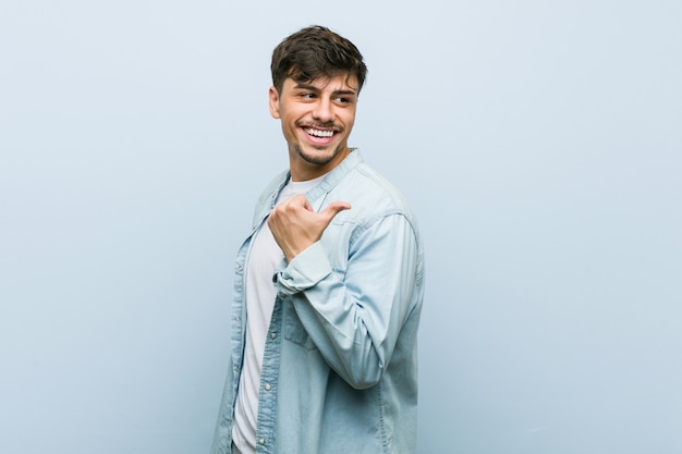 Young hispanic cool man points with thumb finger away, laughing and carefree.