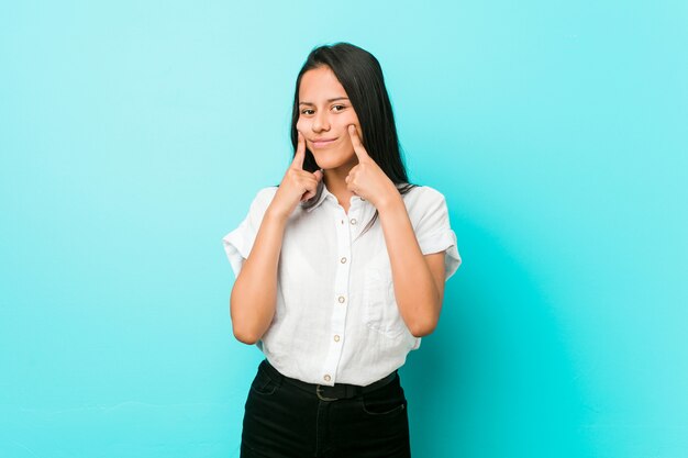 Young hispanic cool woman against a blue wall doubting between two options.