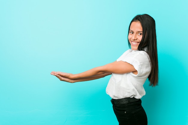 Young hispanic cool woman against a blue wall holding a copy space on a palm.