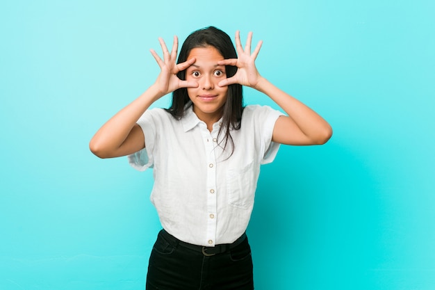 Young hispanic cool woman against a blue wall keeping eyes opened to find a success opportunity.